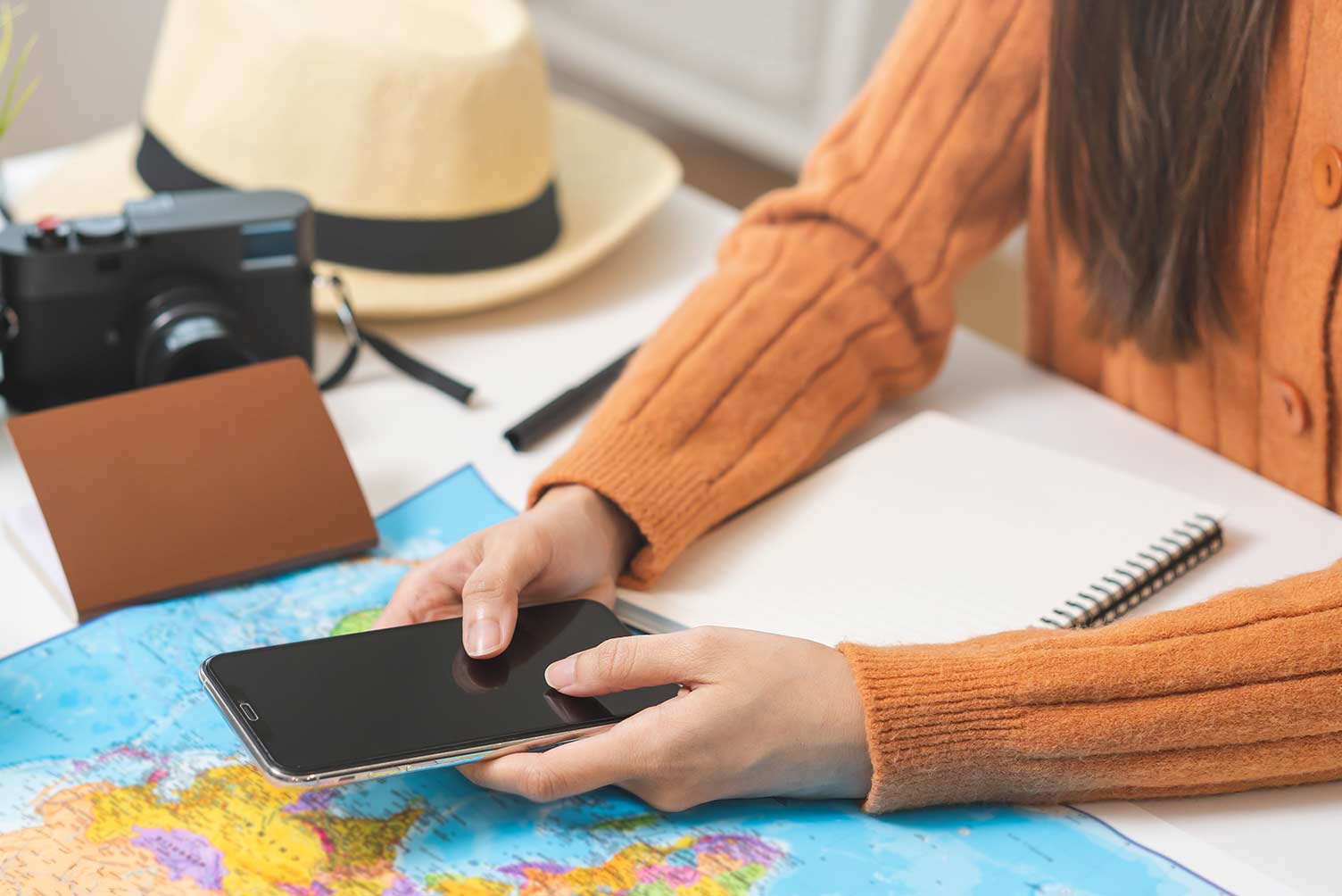 Mujer preparando viaje con teléfono y mapa encima de una mesa