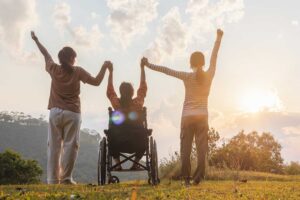 Tres personas con la manos levantadas, una de ellas sentada en silla de ruedas